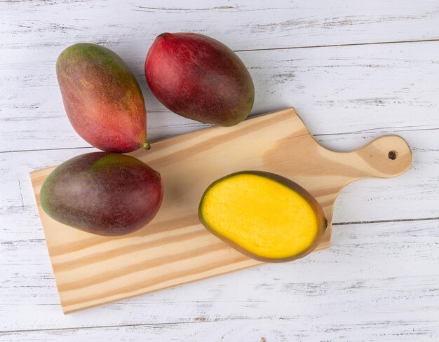 Eine Gruppe reife Mangos mit geschnittenen Früchten über Holzbrett.