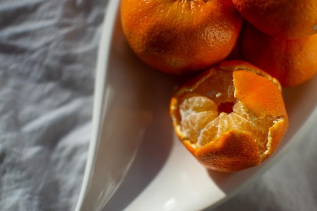 Eine Gruppe reife orangefarbene Mandarinen auf einem weißen Teller auf einem weißen Blatt