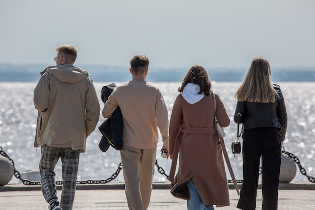 Eine Gruppe stilvoller junger Freunde, Männer und Frauen, die zusammen am Ufer des Meeres spazieren und das Wochenende genießen