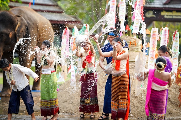 Eine Gruppe thailändischer Frauen und Kinder in thailändischen traditionellen Kleidern spielt zu spritzendem Wasser.