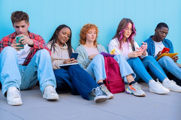 Eine Gruppe verschiedener Jugendlicher sitzt im Freien und benutzt Smartphones und Notebooks