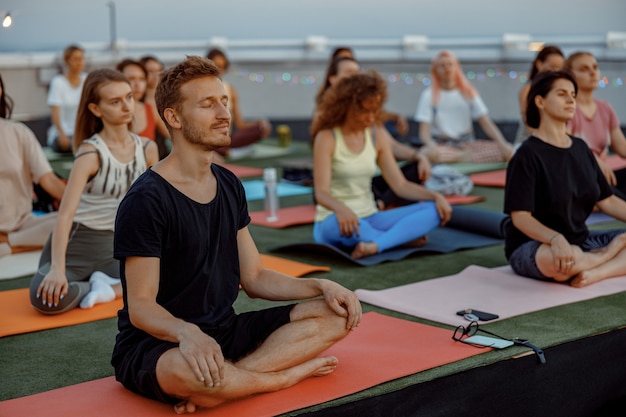 Eine Gruppe verschiedener Menschen praktiziert meditative Yoga-Übungen auf dem Dach an einem wunderschönen Sonnenuntergang am Sommerabend