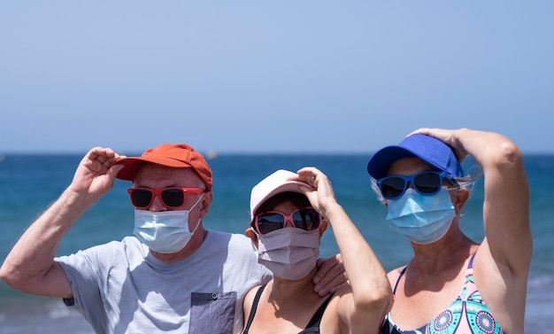 Eine Gruppe von drei älteren Leuten, die Strandferien zusammen mit Hüten genießen