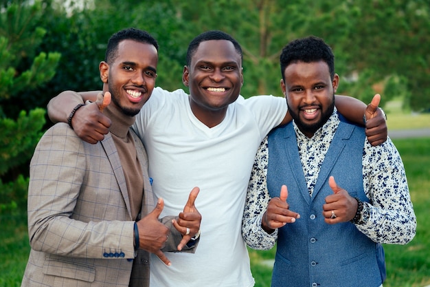Eine Gruppe von drei schwarzen Männern in stilvollen Anzügen trifft sich in einem Sommerpark. Afroamerikaner Freunde hispanischer Geschäftsmann Gruß Pose Teamarbeit im Freien