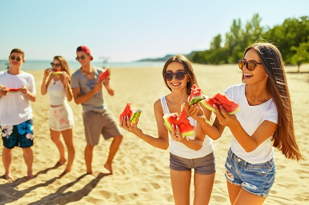 Eine Gruppe von Freunden amüsiert sich beim Wassermelonenessen am Strand. Ausgezeichnetes sonniges Wetter. Super Stimmung im Sommer