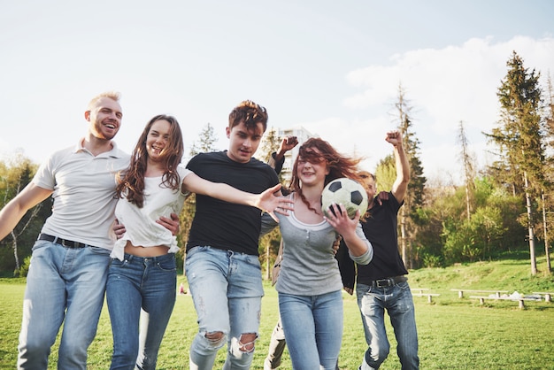 Eine Gruppe von Freunden im Freizeitoutfit spielt Fußball unter freiem Himmel. Die Leute haben Spaß und haben Spaß. Aktive Ruhe und malerischer Sonnenuntergang