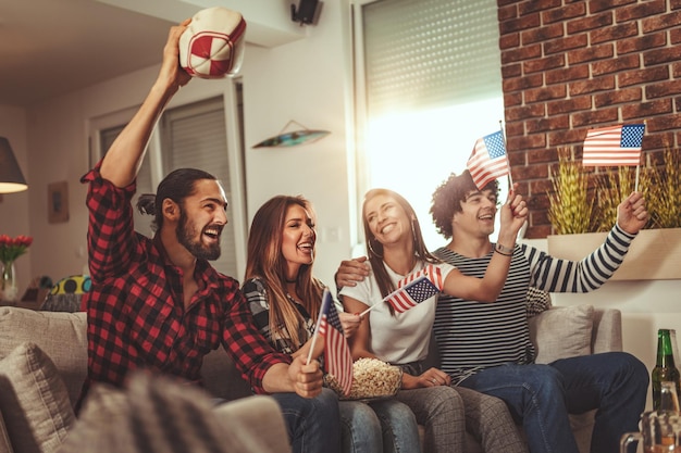 Eine Gruppe von Freunden sieht sich die Übertragung einer Sportveranstaltung an. Sie sitzen im Wohnzimmer vor dem Fernseher, essen Snacks, trinken Bier und feuern die Lieblingsmannschaft an.