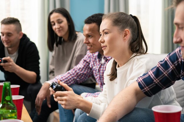 Eine Gruppe von Freunden spielt zu Hause gemeinsam Videospiele und hat Spaß, eine traurige Frau konkurriert mit einer Freundin