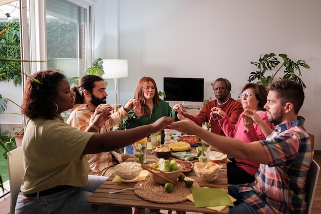 Eine Gruppe von Freunden unterschiedlichen Alters, die sich vor dem Essen die Hände halten und beten.