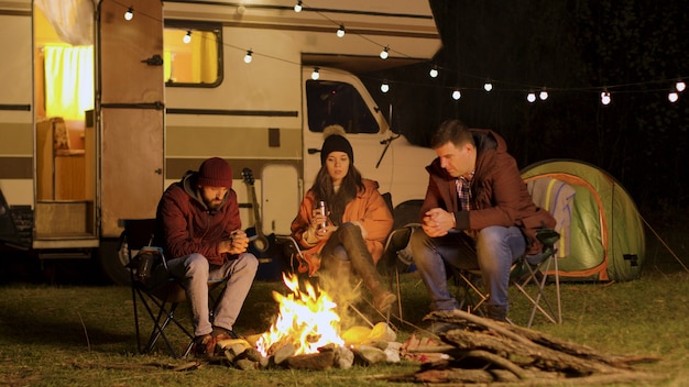 Eine Gruppe von Freunden versammelte sich in einer kalten Herbstnacht um das Lagerfeuer. Nachdenkliche Freunde am Lagerfeuer.