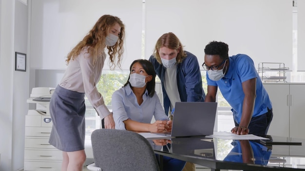 Eine Gruppe von Geschäftsleuten trifft sich und arbeitet am Laptop im Büro und trägt eine Maske