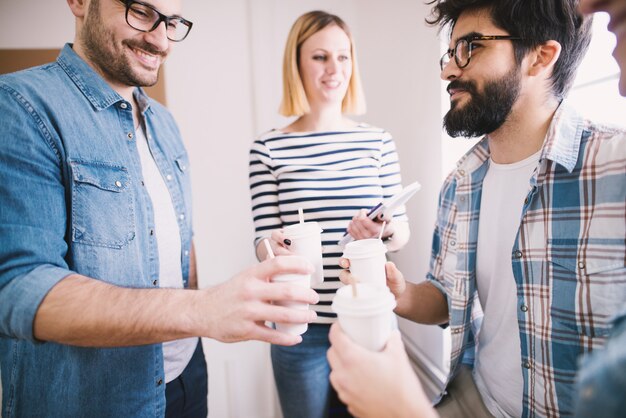 Eine Gruppe von jungen, glücklichen Mitarbeitern trinkt Kaffee in der Pappbecher.