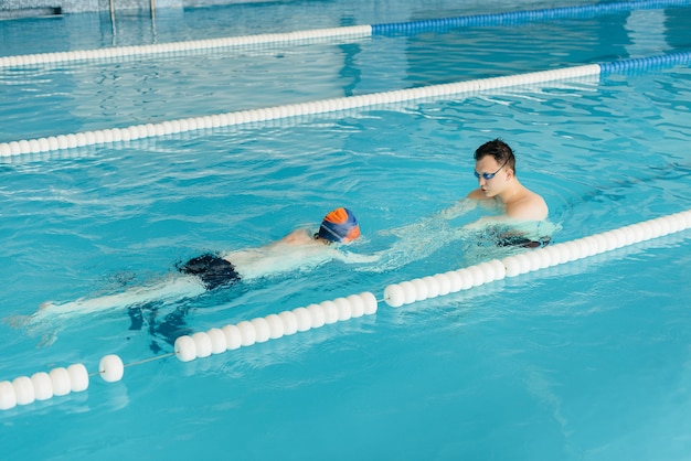 Eine Gruppe von Jungen und Mädchen trainiert und lernt mit einem Lehrer das Schwimmen im Pool. Entwicklung des Kindersports.