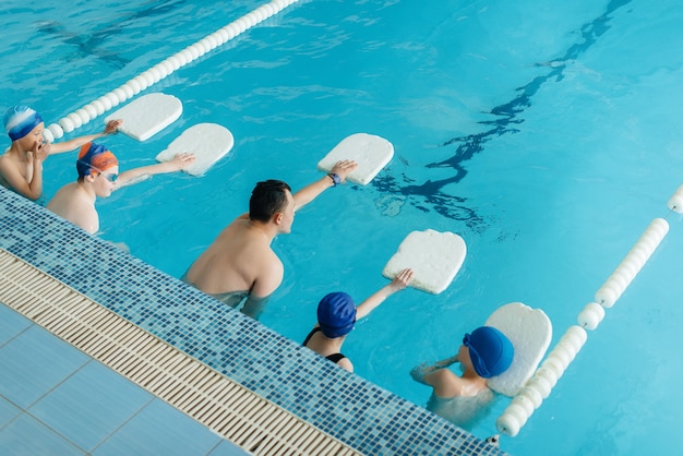 Eine Gruppe von Jungen und Mädchen trainiert und lernt mit einem Lehrer das Schwimmen im Pool. Entwicklung des Kindersports.
