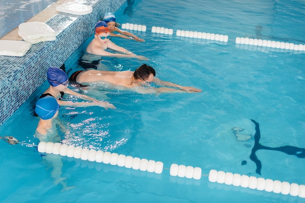 Eine Gruppe von Jungen und Mädchen trainiert und lernt mit einem Lehrer das Schwimmen im Pool. Entwicklung des Kindersports.