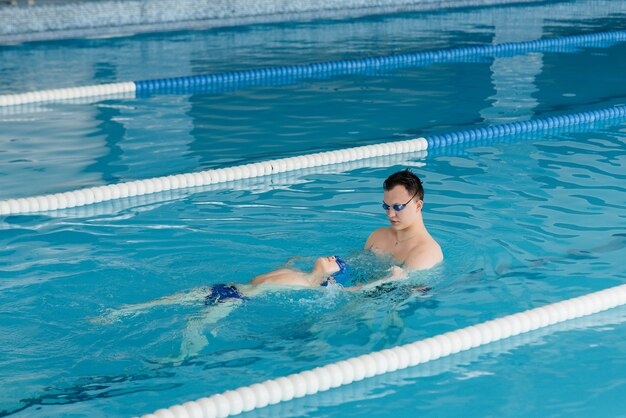 Eine Gruppe von Jungen und Mädchen trainiert und lernt mit einem Lehrer das Schwimmen im Pool. Entwicklung des Kindersports.