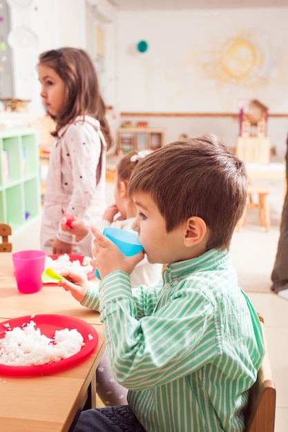 Eine Gruppe von Kindern im Kindergarten sitzt an einem Holztisch und isst Reis