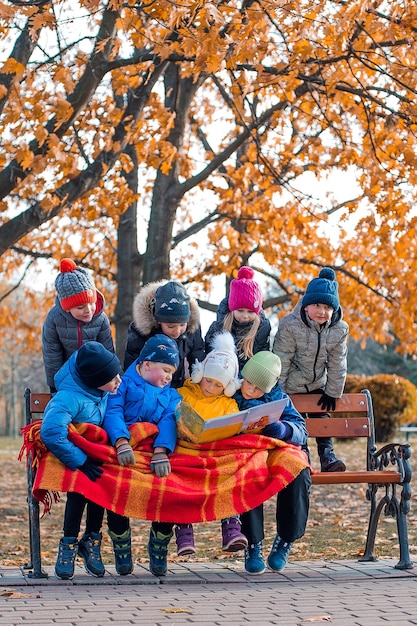 Eine Gruppe von Kindern liest im Herbst auf einer Parkbank ein Buch. Platz für Text