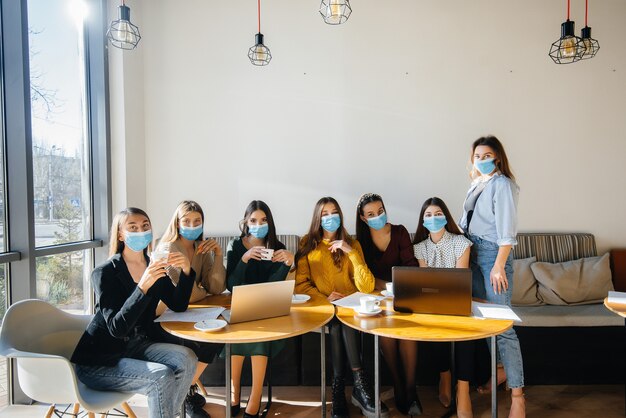 Eine Gruppe von Mädchen in Masken sitzt in einem Café und arbeitet an Laptops. Schüler unterrichten.