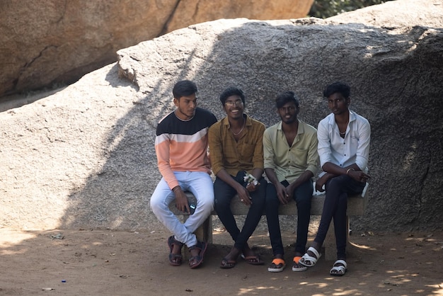 Eine Gruppe von Männern sitzt auf einer Bank vor einem großen Felsen.