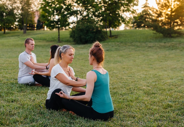 Eine Gruppe von Menschen führt während des Sonnenuntergangs gepaarte Yoga-Übungen in einem Park durch. Gesunder Lebensstil, Meditation und Wellness.