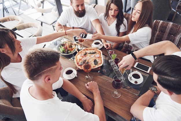 Eine Gruppe von Menschen macht ein Selfie-Foto in einem Café. Die besten Freunde versammelten sich an einem Esstisch, aßen Pizza und sangen verschiedene Getränke