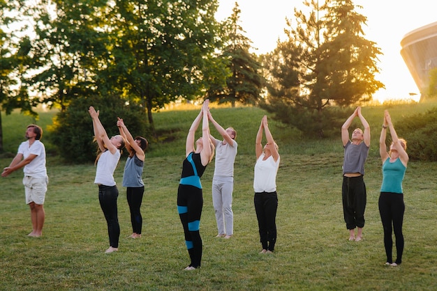 Eine Gruppe von Menschen macht Yoga im Park bei Sonnenuntergang. Gesunder Lebensstil, Meditation und Wellness.