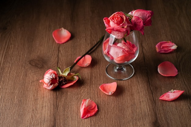 Eine Gruppe von rosa Rosen in Weinglas, die auf dunkle Farbe Holztisch fallen