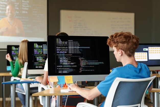 Eine Gruppe von Schülern sitzt an Schreibtischen mit Computern und untersucht im Unterricht Softwarecodes