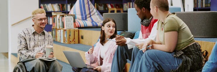 Eine Gruppe von Schülern studiert und diskutiert mit Laptops, Notizbüchern und Stiften in einer modernen Bibliothek