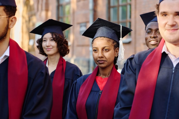 Eine Gruppe von Studenten in Abschlussroben steht draußen und hört dem Dozenten zu