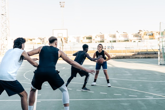 Eine Gruppe von vier Freunden verschiedener Ethnien, die auf einem städtischen Platz Basketball spielen