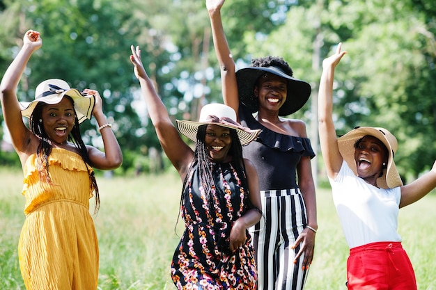 Eine Gruppe von vier wunderschönen afroamerikanischen Frauen trägt einen Sommerhut, der Zeit im grünen Gras im Park verbringt.