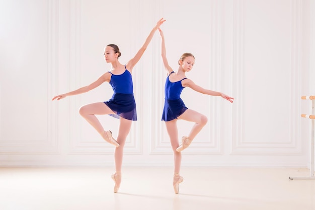 Eine Gruppe von zwei studentischen Ballerinas beschäftigt sich in Spitzenschuhen an der Stange in einem wunderschönen weißen Raum vor dem Hintergrund eines Spiegels