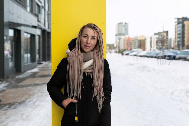 Eine gut gepflegte junge Frau mit blonden Dreadlocks geht in der Kälte die Straße entlang