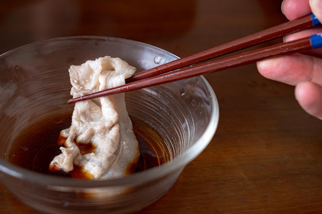 Eine Hand, die Essstäbchen und Essstäbchen über einer Schüssel mit Miso-Sauce hält.