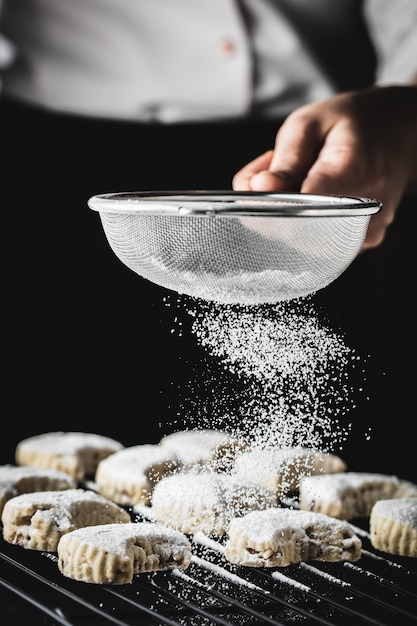 eine Hand, die Zuckerpulver auf leckere traditionelle Kavala-Kekse streut