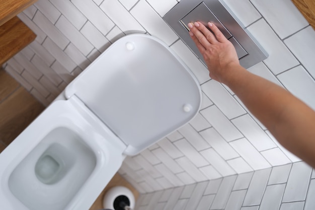 Eine Hand drückt die Spülung der Toilettenschüssel, Nahaufnahme