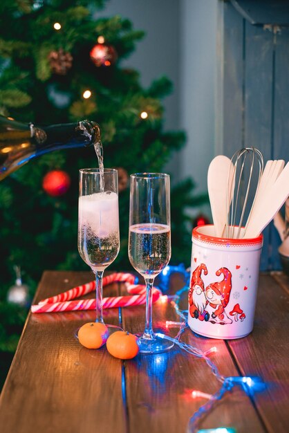 Foto eine hand gießt champagner aus einer flasche in gläser auf dem hintergrund eines weihnachtsbaumes