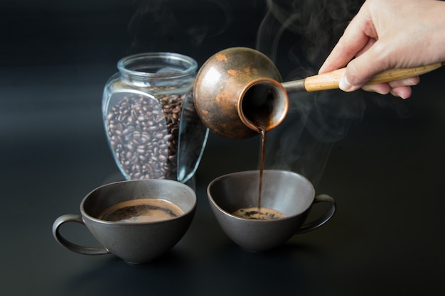 Eine Hand gießt schwarzen Kaffee aus einer alten türkischen Kaffeekanne