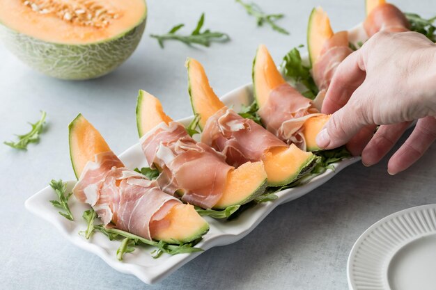 Foto eine hand greift nach einer in schinken gewickelten melonenstücke