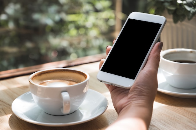 Eine Hand hält ein Smartphone und Kaffeetassen auf dem Tisch