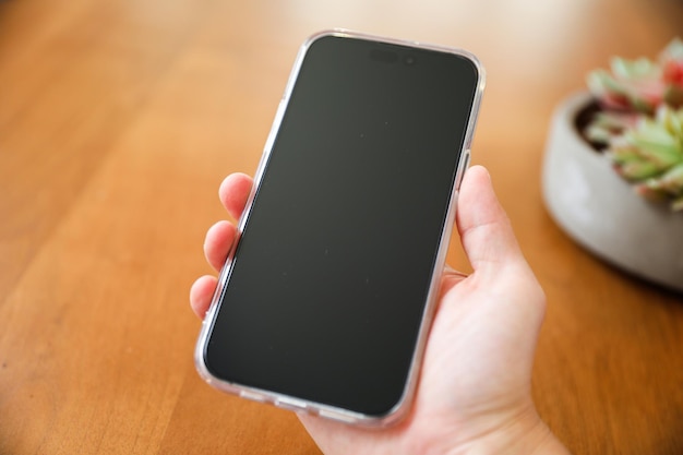 Eine Hand hält ein Telefon mit einer schwarzen Hülle, auf der „iPhone 6“ steht.