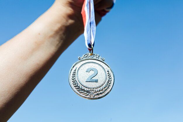 Eine Hand hält eine Silbermedaille auf dem zweiten Platz, mit dem Himmel im Hintergrund. Siegeskonzept