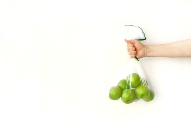 Eine Hand hält eine wiederverwendbare umweltfreundliche Tasche grüne Äpfel auf weißem Hintergrund Zero Waste Shopping