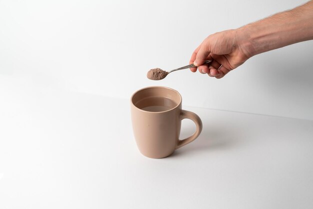 Eine Hand hält einen Löffel mit Kakaopulver und legt ihn in eine Tasse mit heißem Wasser