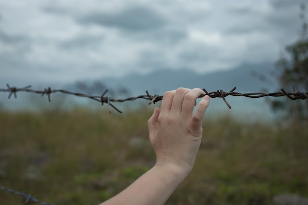 Eine Hand hält sich an Stacheldraht vor einem stürmischen Himmel fest Mann sucht Freiheit hinter dem Zaun