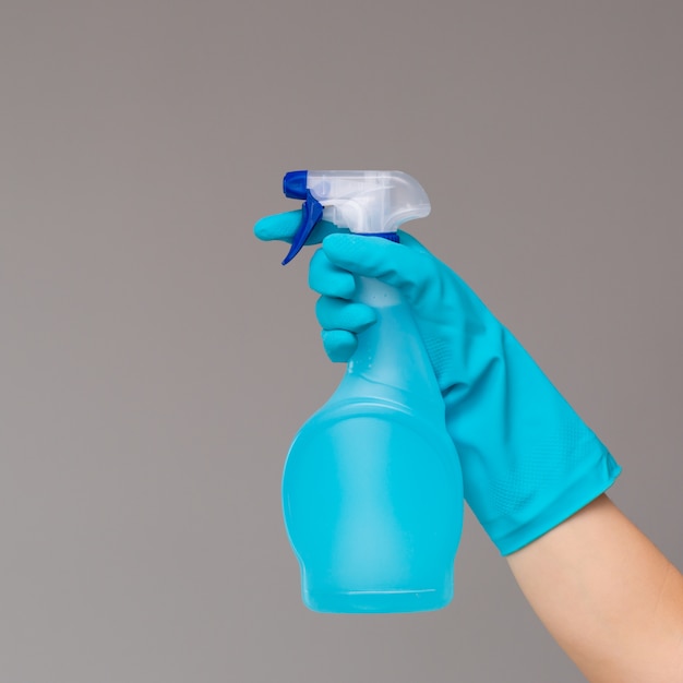 Eine Hand in blauem Gummihandschuh hält den Glasreiniger in einer Sprühflasche. Das Konzept des hellen Frühlinges, Frühjahrsputz.