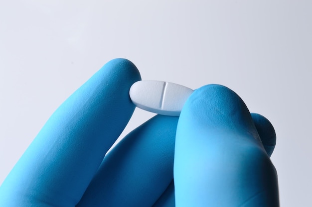 Eine Hand in einem blauen medizinischen Handschuh hält eine weiße Pille in der Nähe