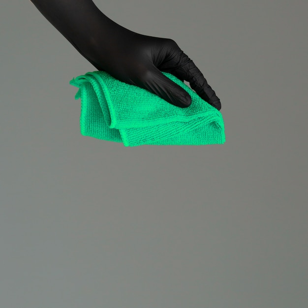 Foto eine hand in einem gummihandschuh hält einen hellen mikrofaserstaubtuch auf einem neutralen hintergrund. konzept des hellen frühlinges, frühjahrsputz.